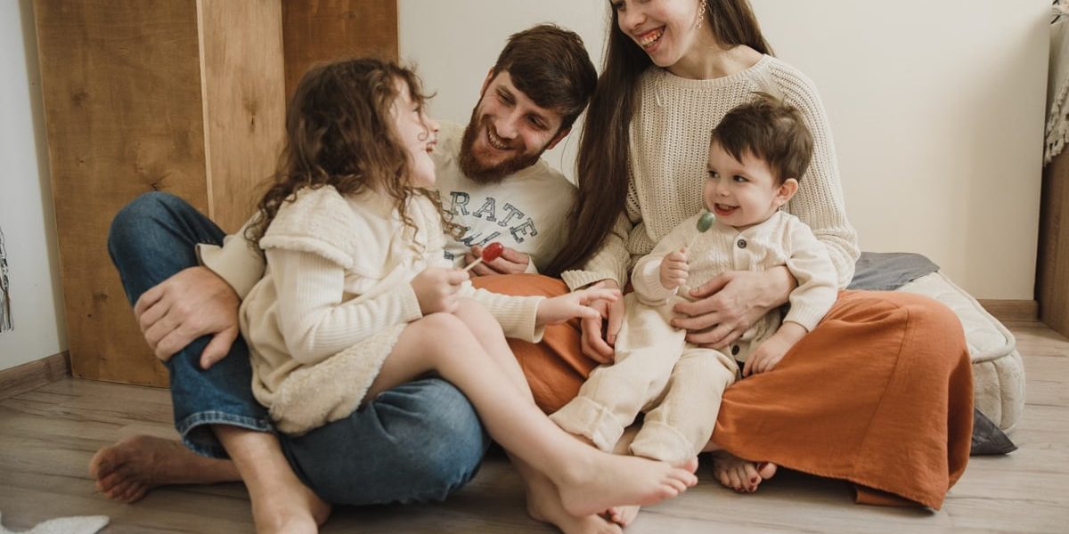 Smiling family of four sitting on the living room floor, enjoying quality time together.