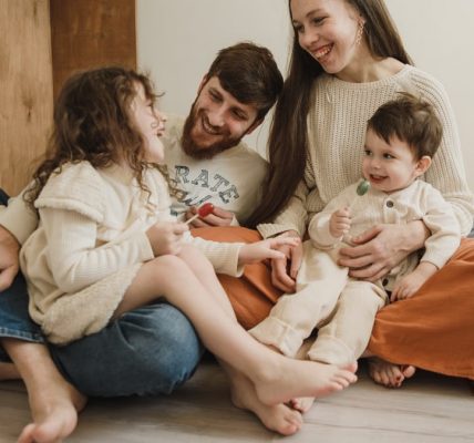 Smiling family of four sitting on the living room floor, enjoying quality time together.