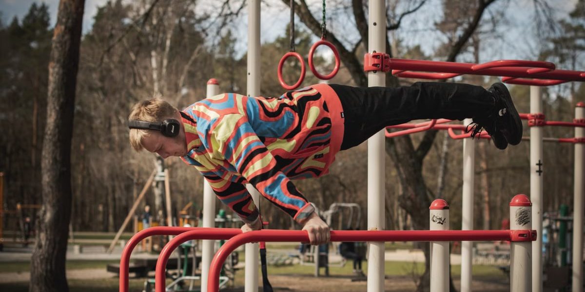Young adult man exercises on outdoor gym bars in a colorful outfit in Vilnius, Lithuania.