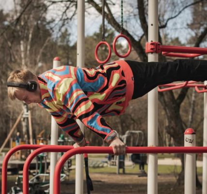 Young adult man exercises on outdoor gym bars in a colorful outfit in Vilnius, Lithuania.