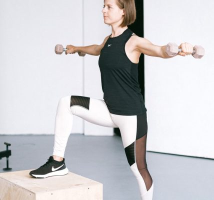 Woman performing fitness exercise with dumbbells in a gym setting, showcasing strength and balance.