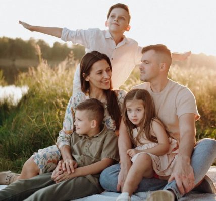 A family of five enjoying a serene picnic in a sunlit meadow during sunset.